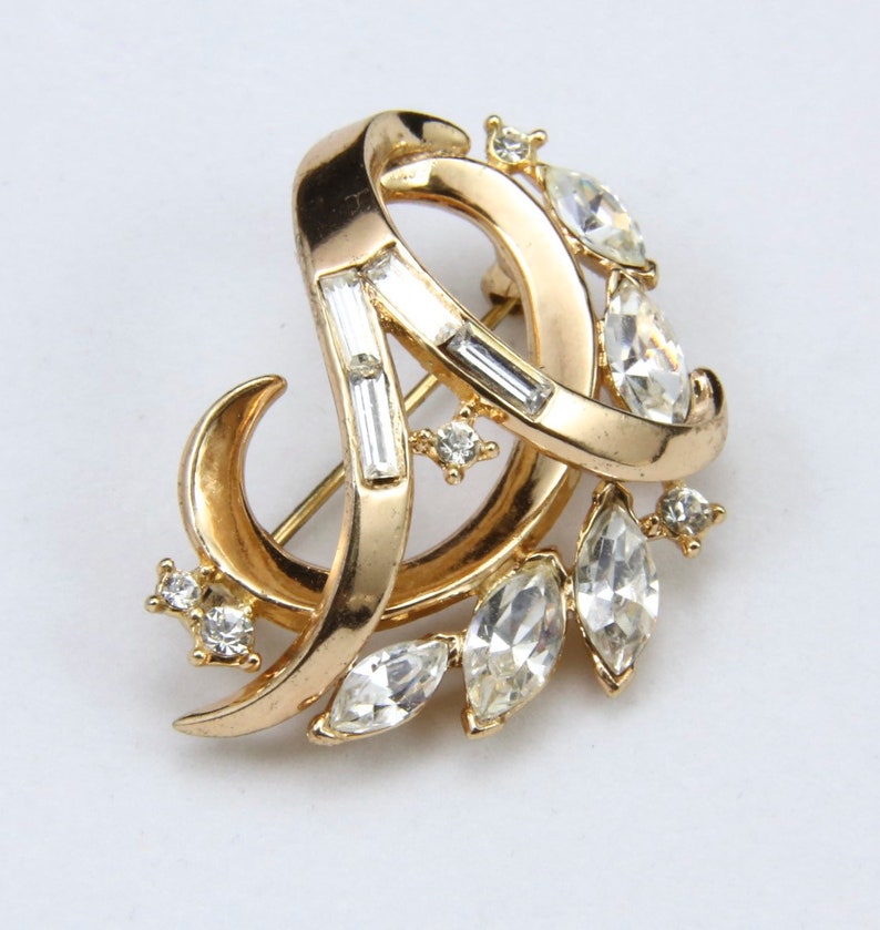 May include: A gold-toned brooch with a swirling design and clear rhinestones.