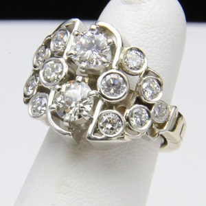 Puede incluir: Un anillo de oro blanco con m&uacute;ltiples diamantes redondos. El anillo tiene un dise&ntilde;o de racimo con diamantes m&aacute;s grandes en el centro y diamantes m&aacute;s peque&ntilde;os alrededor. El anillo se muestra en un dedo.