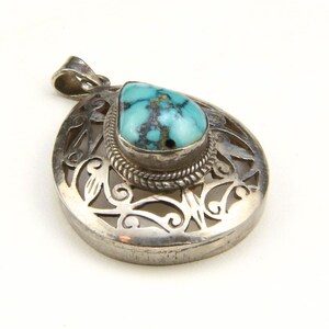 May include: A silver pendant with a turquoise stone. The pendant has an openwork design with a teardrop-shaped turquoise stone at the center. The stone is a vibrant blue-green color with dark veining. The pendant has a loop at the top for a chain.