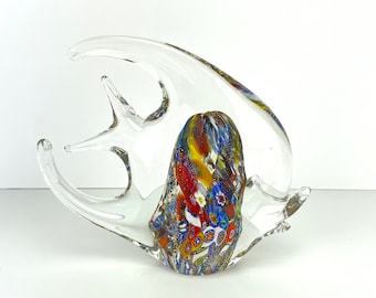 May include: A clear glass fish sculpture with a colorful, patterned body. The sculpture has a large, curved fin design and a central body filled with red, blue, yellow, and white floral patterns. The fish is displayed on a white surface.