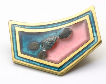 Könnte beinhalten: Abstrakte Brosche mit goldfarbenem Metallrahmen. Die Brosche hat ein zentrales rosa Rechteck, einen türkisblauen Rand und dunkelgraue Akzente. Das Design ist geometrisch und künstlerisch, geeignet, um jedem Outfit einen Hauch von Flair zu verleihen.