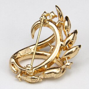 May include: A gold-toned brooch with a floral design. The brooch has a pin on the back and the words "TIFFANY & CO. PAT. PEND." are engraved on the side.