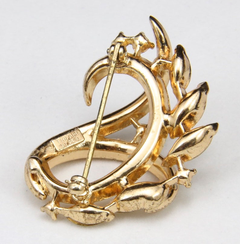 May include: A gold-toned brooch with a floral design. The brooch has a pin on the back and the words "TIFFANY & CO. PAT. PEND." are engraved on the side.