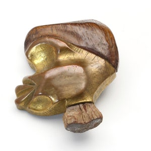 May include: A vintage, abstract sculpture in the shape of a profile. The sculpture features a combination of materials, including a golden-toned metal for the face and a dark brown, wood-like material for the hair. The base is a lighter brown color.