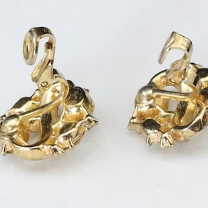 May include: A pair of gold-tone clip-on earrings with a floral design. The earrings have a detailed, intricate design and are made of metal.