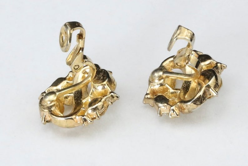 May include: A pair of gold-tone clip-on earrings with a floral design. The earrings have a detailed, intricate design and are made of metal.