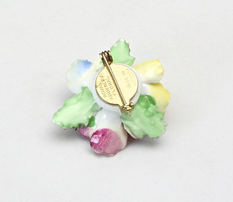 Peut inclure: Une broche en porcelaine en forme de fleur avec un motif floral jaune, rose, bleu et vert. Le dos de la broche a une &eacute;pingle dor&eacute;e et une &eacute;tiquette qui indique "Royal Adderley Floral Made in England".