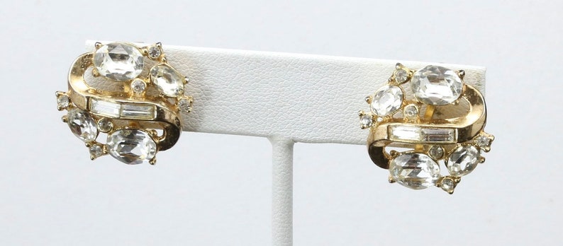 May include: A pair of gold tone clip-on earrings with clear rhinestone accents.