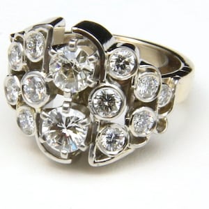 Puede incluir: Un anillo de oro blanco con numerosos diamantes redondos. El anillo tiene un dise&ntilde;o asim&eacute;trico inusual, con diamantes de diferentes tama&ntilde;os agrupados. Los diamantes brillan sobre el metal blanco.