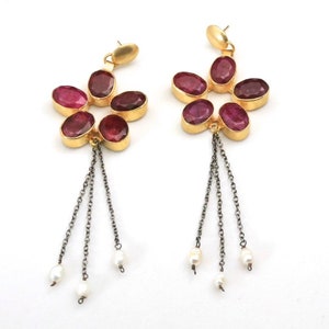 May include: Gold earrings with a flower design featuring red gemstones and a dangling chain with pearls.