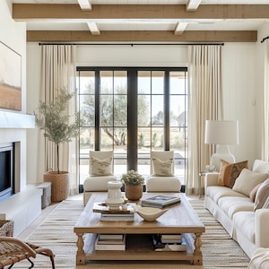 Op de afbeelding: Een woonkamer met een groot raam, een witte bank, een salontafel met boeken en een kom, en twee stoelen met kussens.