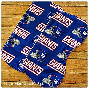 May include: Two blue fabric burp cloths with a white and red pattern of the New York Giants logo and the word "Giants".