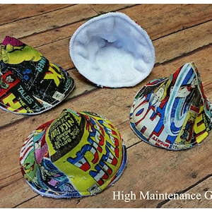May include: Four cone-shaped fabric burp cloths with a white fleece lining. The fabric features a vintage comic book print with colorful images of superheroes. The text on the fabric includes "Tales to the Inc", "Nick Fury", "Against", "Battles", "1606HTY", "HOM", "INCE", "K", "INER", and "TH".
