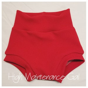 May include: Red high-waisted shorts with a textured fabric. The shorts have a wide waistband and a relaxed fit.