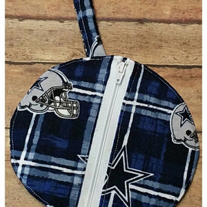 May include: A round, blue and white zippered pouch with a plaid pattern and a Dallas Cowboys logo. The pouch has a loop handle at the top.