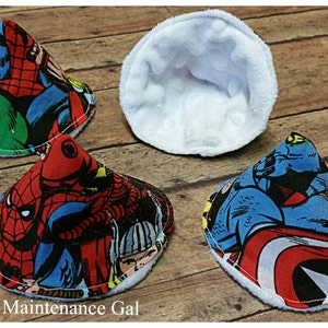 May include: Four cone-shaped fabric burp cloths with a white fleece backing. The fabric features a comic book style print of various superheroes, including Spiderman, Hulk, Captain America, and Thor.