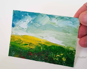May include: A miniature landscape painting depicting a field of yellow and green with a blue sky. The artwork features textured brushstrokes and small red accents. The artist's signature is visible in the lower right corner.