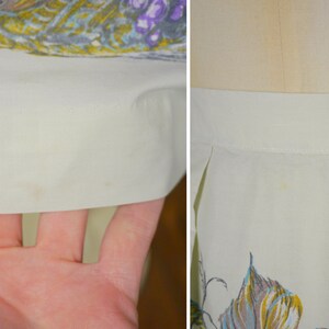May include: Close-up of a white skirt with a floral print. The skirt has a waistband and pleats. There are some light stains on the fabric.