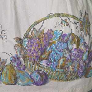 May include: A white fabric with a printed design of a basket overflowing with purple and blue grapes, pears, and other fruits. The basket is woven with brown and gold strands.
