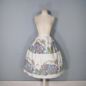 May include: A white full skirt with a grape and fruit print. The skirt has a gathered waist and a full, flowing silhouette.
