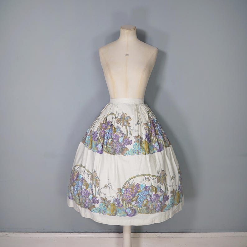 May include: A white full skirt with a grape and fruit print. The skirt has a gathered waist and a full, flowing silhouette.