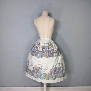 May include: A white skirt with a full gathered skirt silhouette. The skirt has a colorful print of fruit and grapes.