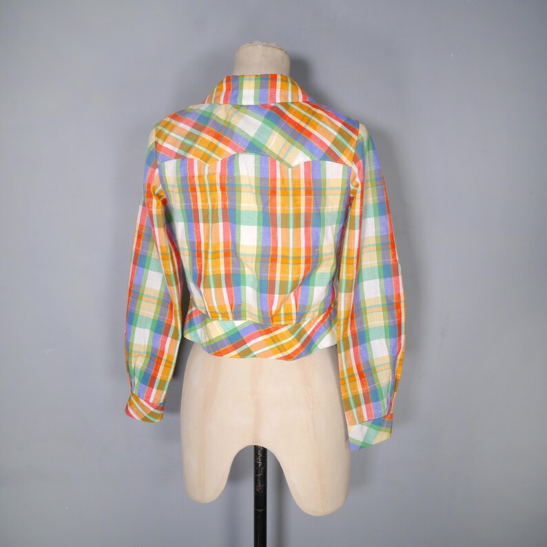 May include: A colorful plaid shirt in a variety of colors, including orange, yellow, green, and blue. The long-sleeved shirt is displayed on a mannequin. The shirt has a button-down front and a collar.