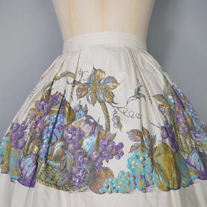 May include: A white full skirt with a vintage floral print featuring grapes, leaves, and fruit. The print is in shades of purple, blue, green, and brown.