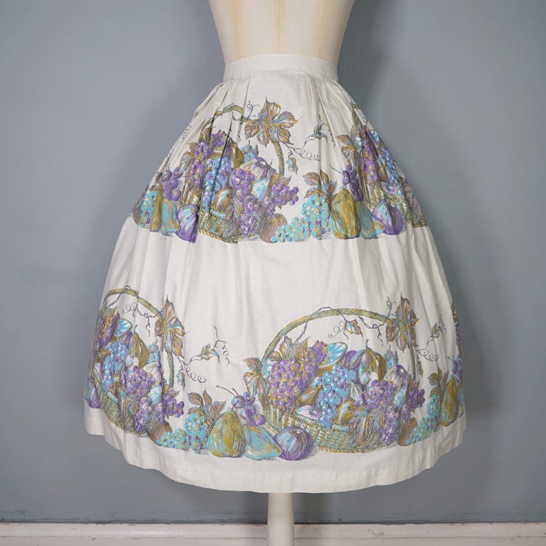 May include: A white full skirt with a purple, green, and brown fruit print. The skirt has a gathered waist and a full, flowing silhouette.