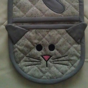 Pode incluir: Luva de forno acolchoada cinza em forma de gato, com nariz rosa e olhos pretos.