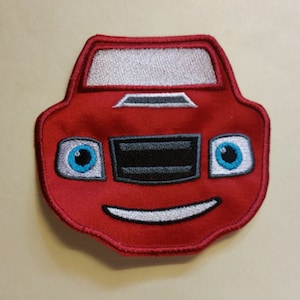 Può includere: Macchina rossa dei cartoni animati con un viso sorridente, occhi blu e un parabrezza bianco. La macchina è ricamata su una toppa di tessuto rosso.