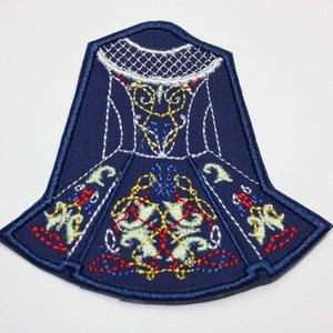 May include: A blue embroidered patch depicting a traditional Irish dress with intricate floral and geometric designs in white, yellow, red, and green thread.