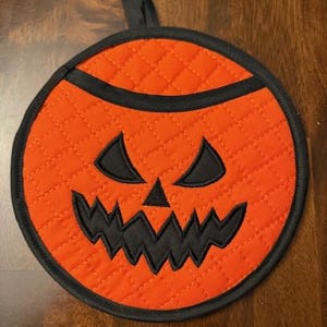 May include: Orange and black quilted hot pad with a stitched jack-o'-lantern face.
