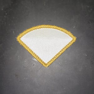May include: A white fabric patch with a yellow stitched border in the shape of a diamond.