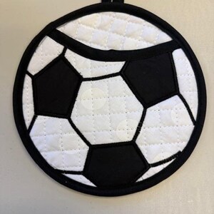 May include: A white and black quilted pot holder shaped like a soccer ball with a hanging loop.
