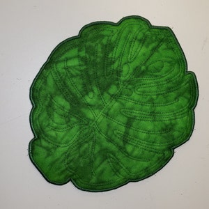 Könnte beinhalten: Ein grünes Filz-Monstera-Blatt mit einem gestickten Umriss. Das Blatt ist hellgrün mit einem dunkelgrünen Umriss.