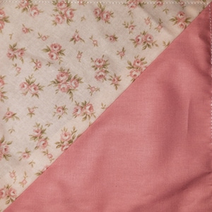 May include: A fabric square with a diagonal seam. One side is a light pink with a small floral pattern. The other side is a solid, darker pink.