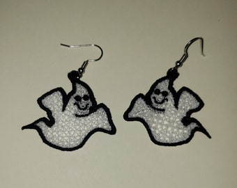 May include: A pair of silver dangle earrings with white ghost-shaped charms. The ghosts have black outlines and smiling faces.