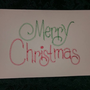 May include: A white card with the words "Merry Christmas" written in green and red thread.