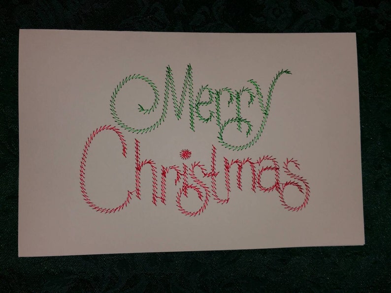 May include: A white card with the words "Merry Christmas" written in green and red thread.