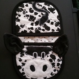May include: Black and white cow-print pot holder with a black and white cow face in the center. The pot holder has a loop for hanging.