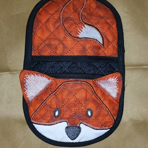 May include: A quilted orange and white fox pot holder with a black border. The fox's tail is curled up on the back of the pot holder.