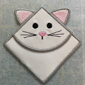 Op de afbeelding: Witte vilt kattenbladwijzer met roze oren en neus, zwarte ogen en snorharen, en grijze stiksels rond de randen.