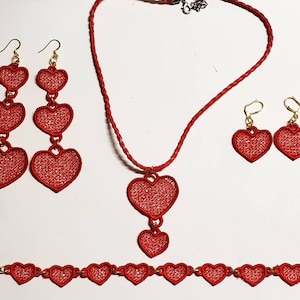 Può includere: Set di gioielli a forma di cuore rosso con collana, orecchini e braccialetto. La collana ha un cuore grande unico con due cuori più piccoli che pendono. Gli orecchini sono ciascuno un solo cuore, e il braccialetto ha una fila di cuori piccoli.
