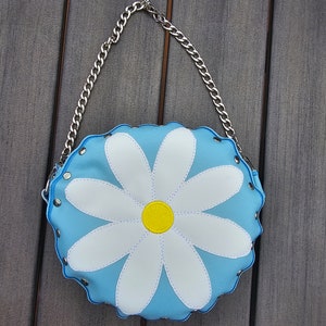 May include: A light blue round purse with a white daisy design and a silver chain strap.