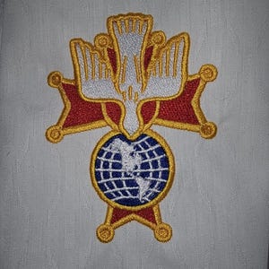 May include: Embroidered patch with a white dove with outstretched wings, a red and gold star, and a blue globe with white continents. The dove is centered above the globe and star.