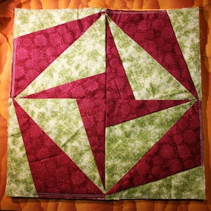 Könnte beinhalten: Ein Quiltblock mit geometrischem Design, das abwechselnd rote und grüne Stoffquadrate zeigt. Der Stoff hat ein Blumenmuster.