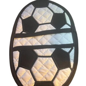 May include: A white and black quilted pot holder with a soccer ball design. The pot holder has a loop for hanging.