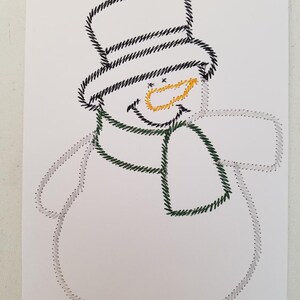 May include: A white paper card with a black and white stitched snowman design. The snowman has a black top hat, a green scarf, and a yellow stitched smile.