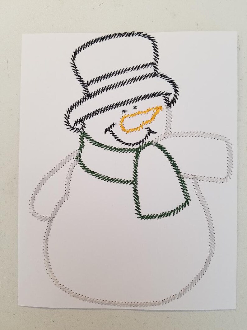May include: A white paper card with a black and white stitched snowman design. The snowman has a black top hat, a green scarf, and a yellow stitched smile.